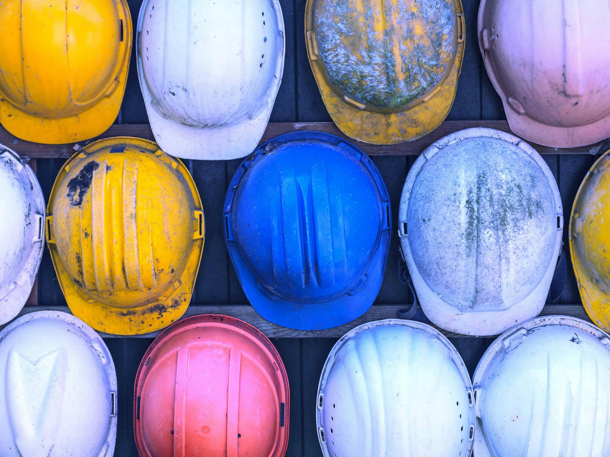 A collection of hard hats in various colors and states of wear, hanging on a wall.