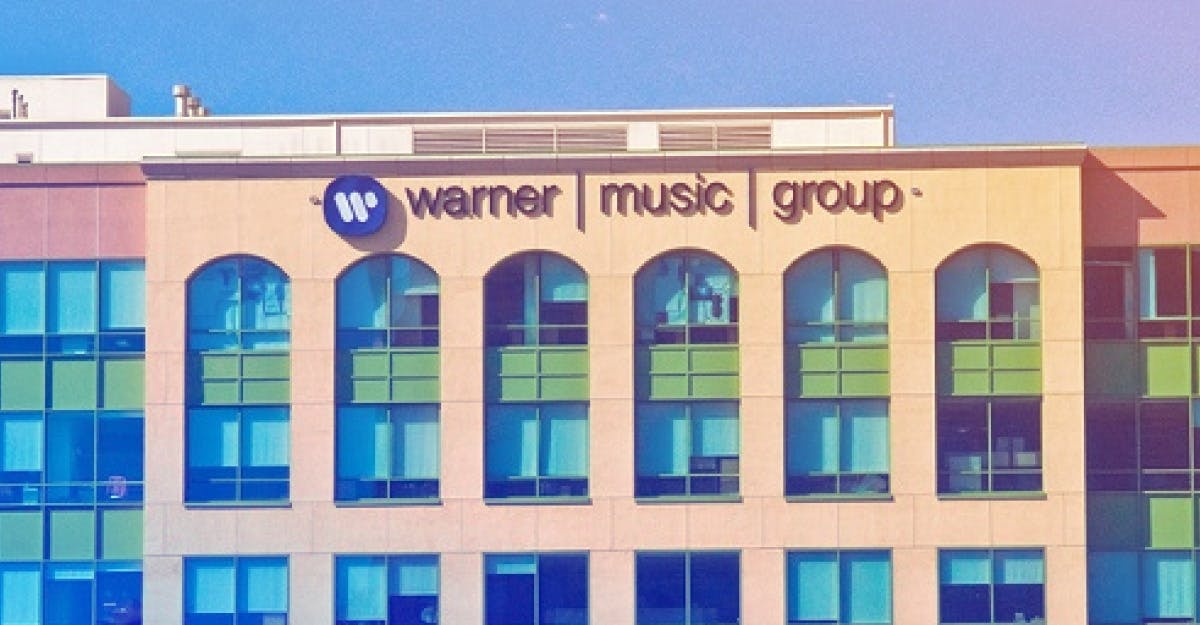 Exterior view of the Warner Music Group building, showcasing its peach-colored facade, multiple arched windows, and prominent signage displaying the company's logo and name.