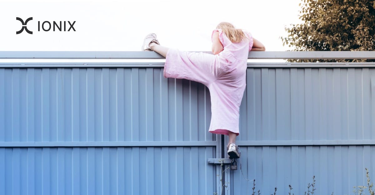 A person in pink overalls climbs over a light blue metal fence.