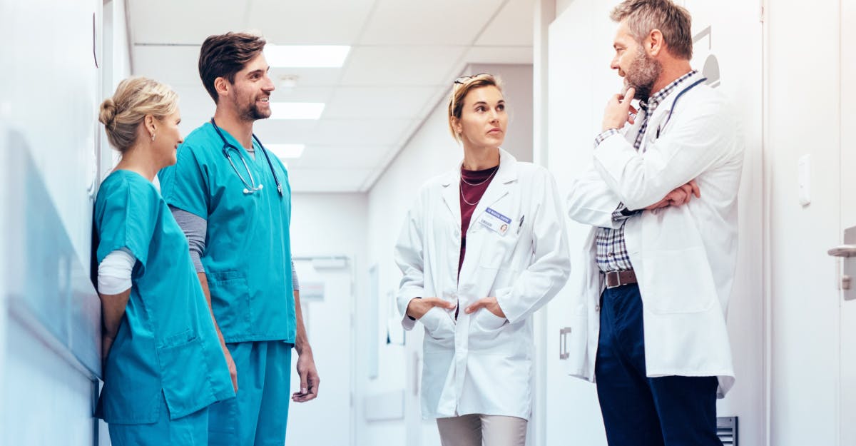 Four medical professionals, two women and two men, stand in a hospital hallway engaged in conversation.